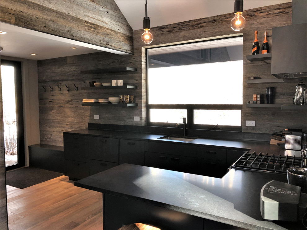 Example of a mid-sized trendy u-shaped light wood floor, orange floor and vaulted ceiling open concept kitchen design in Other with an undermount sink, flat-panel cabinets, black cabinets, brown backsplash, stainless steel appliances, a peninsula and brown countertops