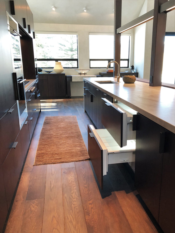 Photo of a large contemporary galley open plan kitchen in Other with a submerged sink, flat-panel cabinets, dark wood cabinets, coloured appliances, medium hardwood flooring, an island, brown floors, multicoloured worktops and a vaulted ceiling.