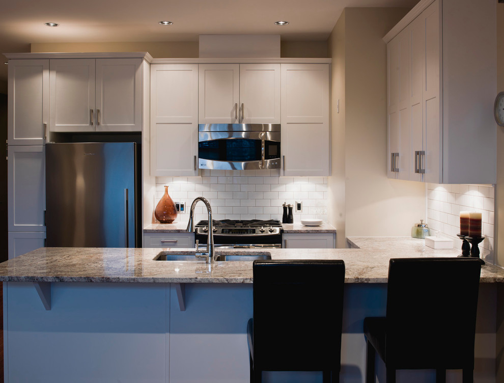 This is an example of a small contemporary u-shaped kitchen/diner in Toronto with a submerged sink, shaker cabinets, white cabinets, granite worktops, white splashback, metro tiled splashback, stainless steel appliances and light hardwood flooring.
