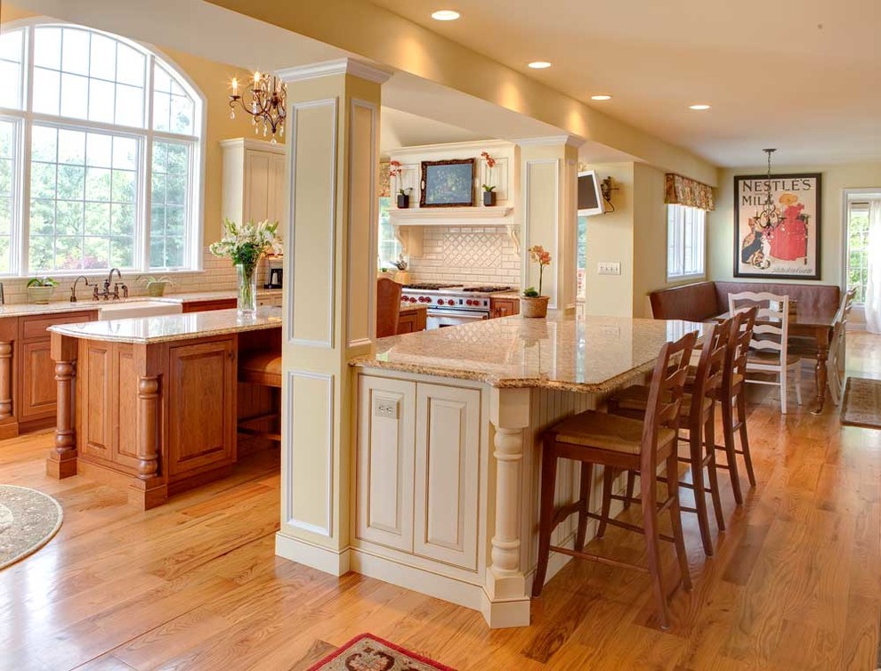 Large elegant l-shaped light wood floor and beige floor open concept kitchen photo in Philadelphia with a farmhouse sink, raised-panel cabinets, white cabinets, granite countertops, white backsplash, subway tile backsplash, stainless steel appliances and two islands