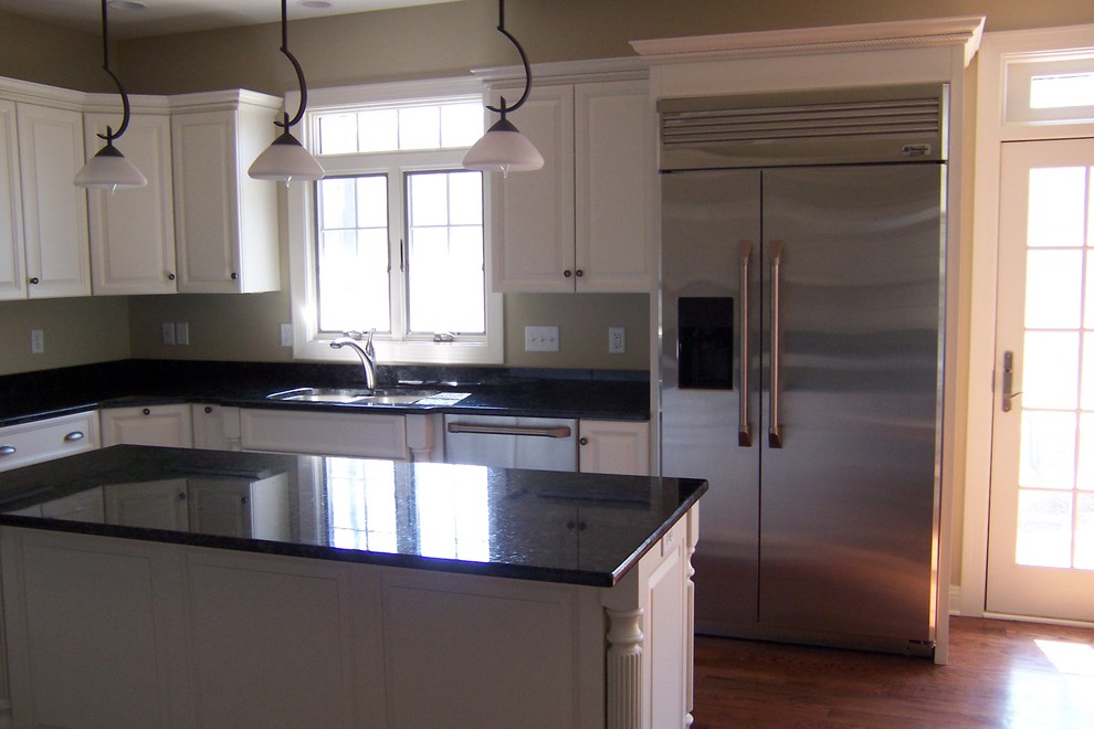 Klassisk inredning av ett kök och matrum, med en undermonterad diskho, luckor med upphöjd panel, vita skåp, granitbänkskiva, rostfria vitvaror, mellanmörkt trägolv och en köksö