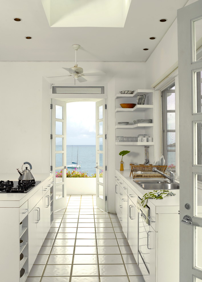 На фото: параллельная кухня в морском стиле с плоскими фасадами, двойной мойкой, белыми фасадами, столешницей из ламината, полом из керамической плитки и островом