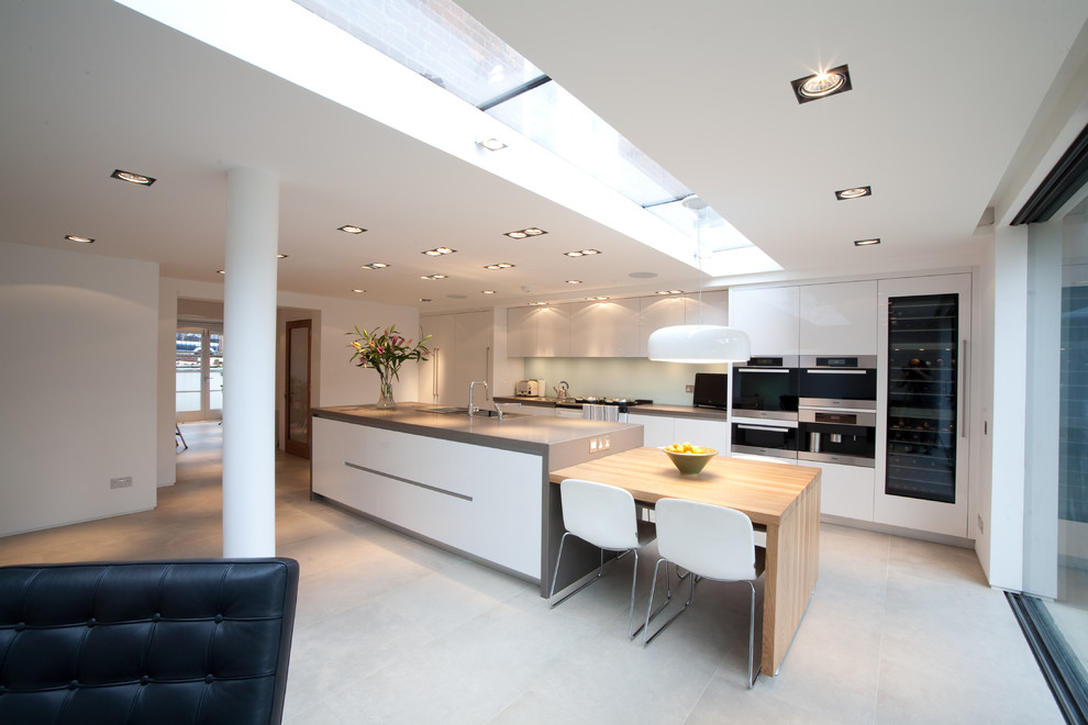 Einzeilige, Große Moderne Küche mit flächenbündigen Schrankfronten, weißen Schränken, Betonarbeitsplatte, Rückwand aus Glasfliesen, Halbinsel und grauem Boden in Sussex