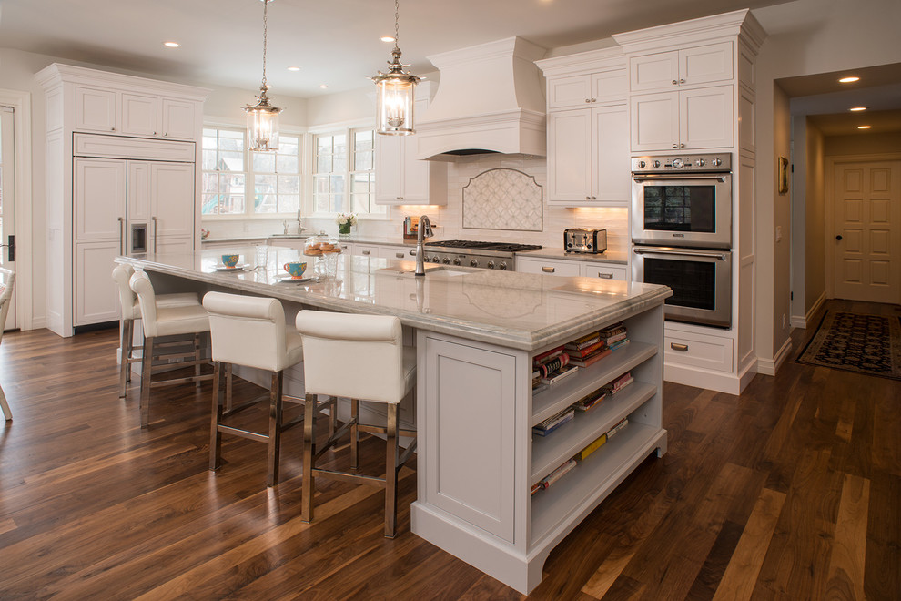 This is an example of a classic l-shaped open plan kitchen in Denver with a submerged sink, beaded cabinets, white cabinets, white splashback, stainless steel appliances, medium hardwood flooring and an island.