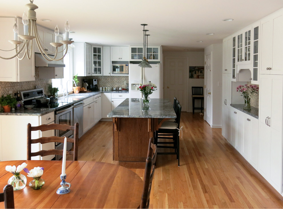 Eat-in kitchen - mid-sized l-shaped medium tone wood floor eat-in kitchen idea in Providence with an undermount sink, white cabinets, granite countertops, stainless steel appliances, an island, recessed-panel cabinets, multicolored backsplash and porcelain backsplash