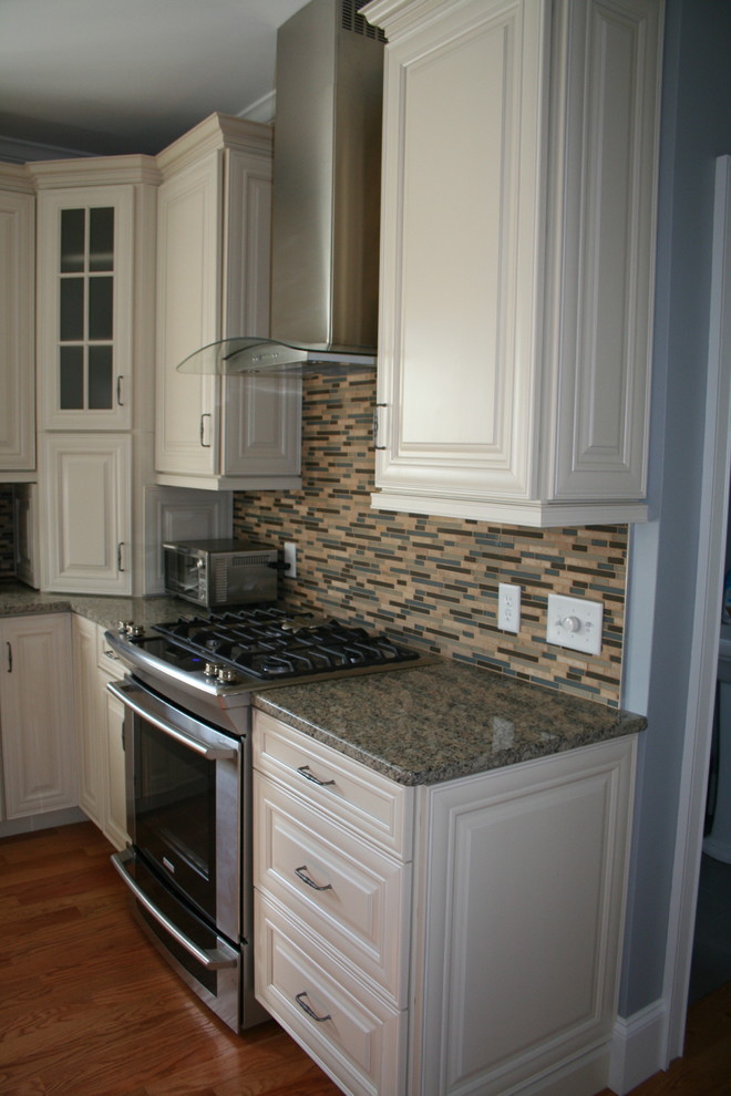 Klassisk inredning av ett mellanstort kök, med en undermonterad diskho, luckor med upphöjd panel, vita skåp, granitbänkskiva, flerfärgad stänkskydd, rostfria vitvaror, mellanmörkt trägolv och en köksö