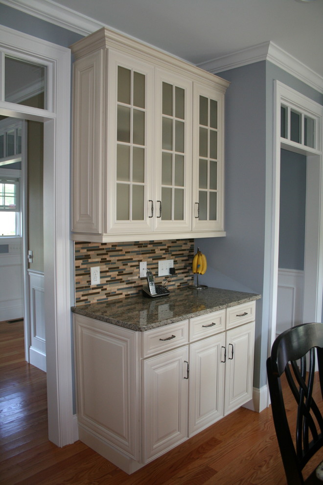 Eat-in kitchen - mid-sized traditional l-shaped medium tone wood floor eat-in kitchen idea in Providence with an undermount sink, raised-panel cabinets, white cabinets, granite countertops, multicolored backsplash, mosaic tile backsplash, stainless steel appliances and an island