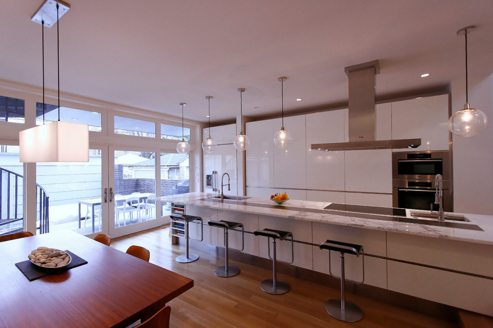 Photo of a medium sized modern galley kitchen/diner in Chicago with a submerged sink, flat-panel cabinets, white cabinets, marble worktops, light hardwood flooring and an island.