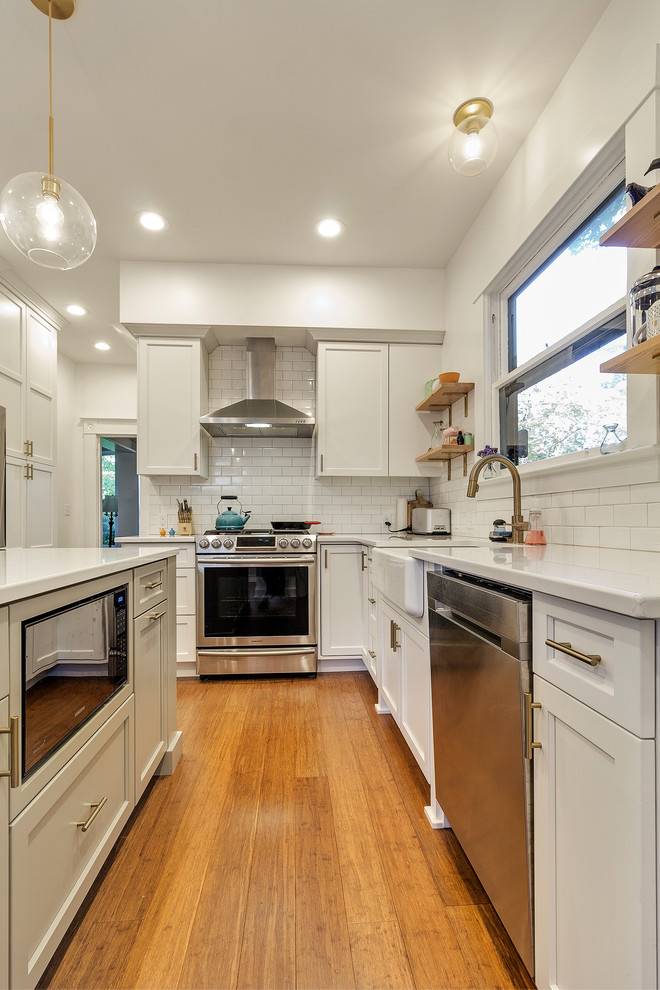 Idéer för att renovera ett stort amerikanskt vit vitt kök, med en rustik diskho, skåp i shakerstil, vita skåp, bänkskiva i kvarts, vitt stänkskydd, stänkskydd i porslinskakel, rostfria vitvaror, bambugolv, en köksö och brunt golv