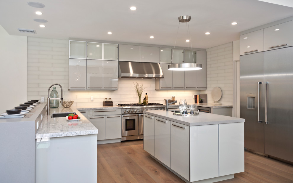 Contemporary u-shaped kitchen in Los Angeles with a submerged sink, flat-panel cabinets, white cabinets, white splashback, stainless steel appliances, light hardwood flooring and an island.
