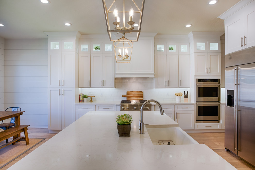 Example of a large transitional l-shaped light wood floor eat-in kitchen design in Phoenix with an undermount sink, shaker cabinets, white backsplash, stainless steel appliances, an island, white cabinets and ceramic backsplash
