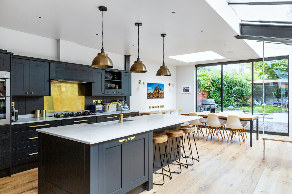 ロンドンにあるトランジショナルスタイルのおしゃれなキッチン (エプロンフロントシンク、シェーカースタイル扉のキャビネット、黒いキャビネット、黄色いキッチンパネル、シルバーの調理設備、無垢フローリング、茶色い床、白いキッチンカウンター) の写真