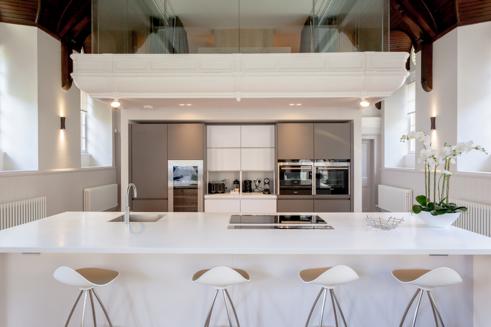 Inspiration for a contemporary galley kitchen in Edinburgh with a submerged sink, flat-panel cabinets, grey cabinets, stainless steel appliances, an island, white worktops and a vaulted ceiling.