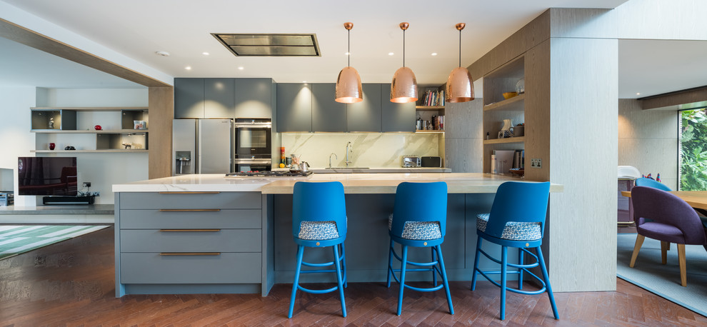 Inspiration for a contemporary galley open plan kitchen in London with flat-panel cabinets, blue cabinets, white splashback, black appliances, dark hardwood flooring, a breakfast bar, brown floors and white worktops.