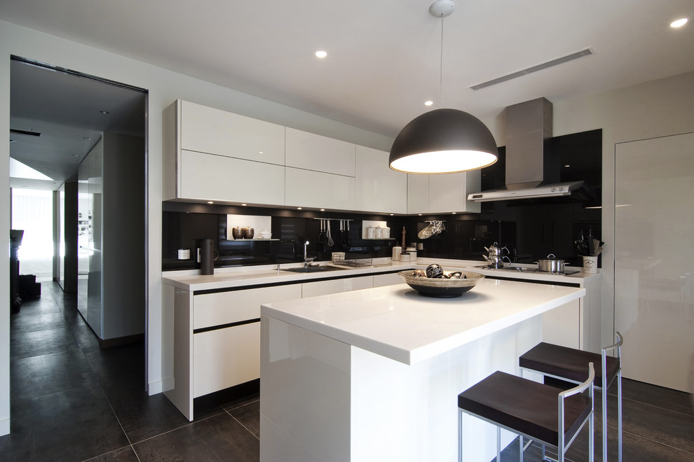 Moderne Küche in L-Form mit Unterbauwaschbecken, flächenbündigen Schrankfronten, weißen Schränken und Küchenrückwand in Schwarz in Sonstige