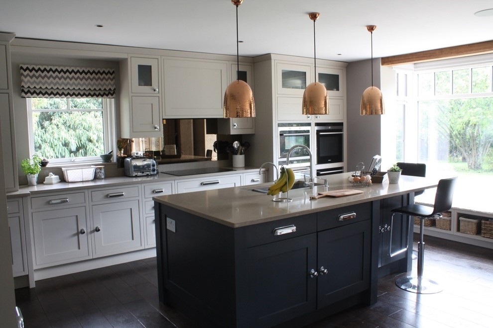 Inspiration for a large traditional l-shaped kitchen/diner in Hertfordshire with a submerged sink, shaker cabinets, beige cabinets, engineered stone countertops, metallic splashback, glass sheet splashback, stainless steel appliances, dark hardwood flooring and an island.