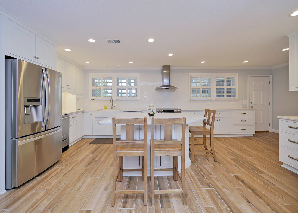 Large nautical u-shaped kitchen in Jacksonville with a belfast sink, recessed-panel cabinets, white cabinets, engineered stone countertops, white splashback, metro tiled splashback, stainless steel appliances, porcelain flooring and multi-coloured floors.