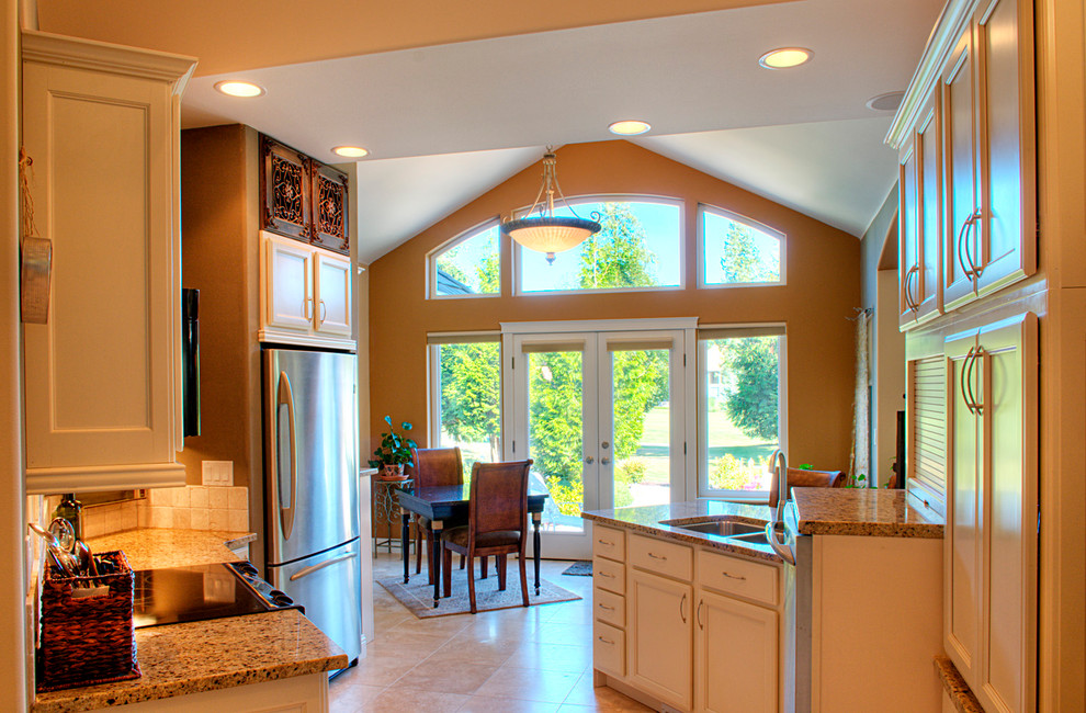 Bild på ett mellanstort funkis kök och matrum, med en trippel diskho, luckor med infälld panel, vita skåp, granitbänkskiva, vitt stänkskydd, stänkskydd i stenkakel, rostfria vitvaror, klinkergolv i keramik och en halv köksö