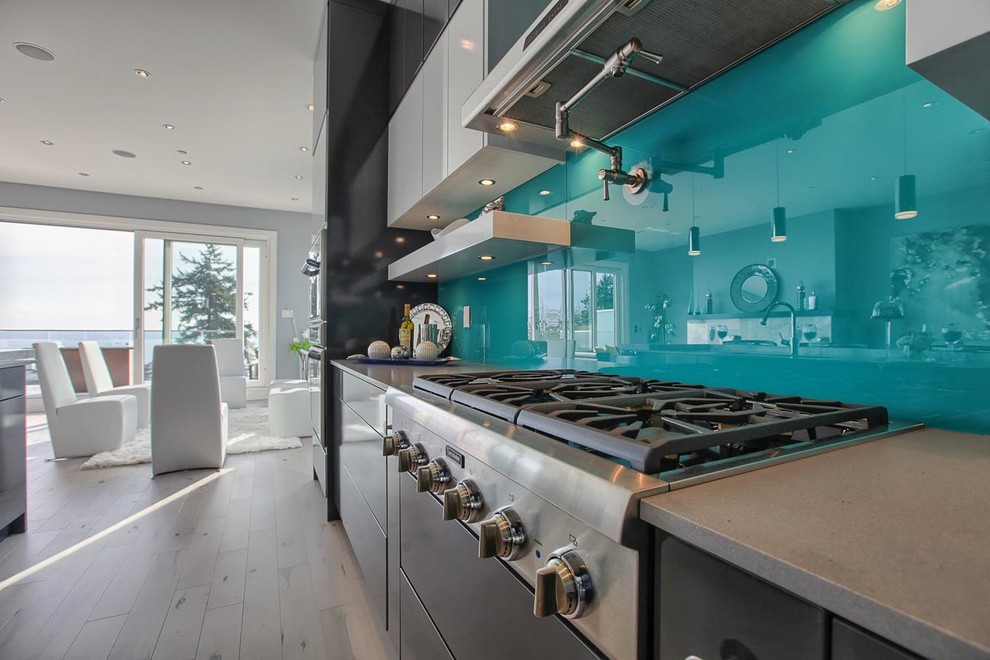 Mid-sized trendy l-shaped light wood floor and gray floor open concept kitchen photo in Vancouver with flat-panel cabinets, black cabinets, quartz countertops, blue backsplash, glass sheet backsplash, stainless steel appliances and an island