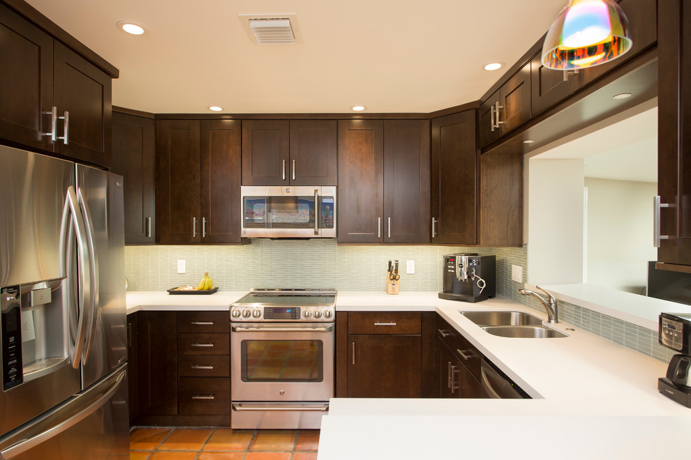 Photo of a medium sized contemporary u-shaped kitchen/diner in Miami with a double-bowl sink, shaker cabinets, brown cabinets, quartz worktops, green splashback, glass tiled splashback, stainless steel appliances, terracotta flooring and an island.