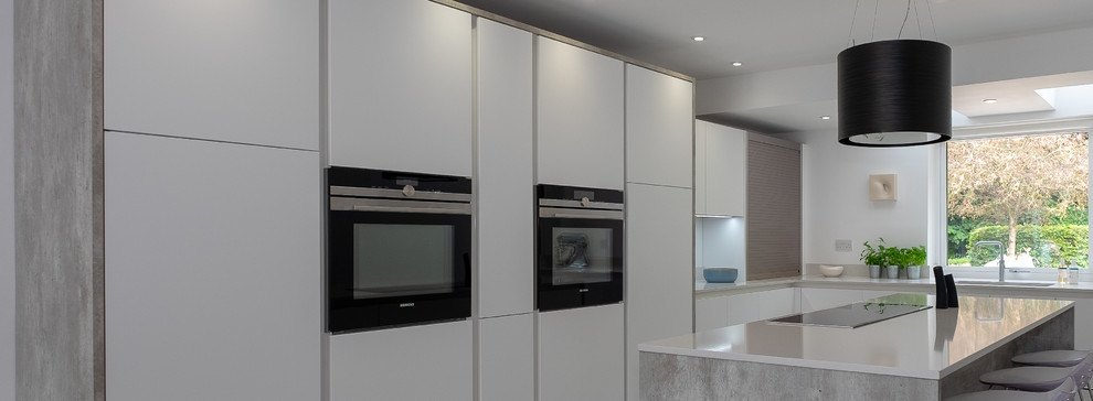 Bild på ett mellanstort industriellt vit vitt kök, med en undermonterad diskho, släta luckor, vita skåp, bänkskiva i kvartsit, vitt stänkskydd, rostfria vitvaror, linoleumgolv, en köksö och flerfärgat golv