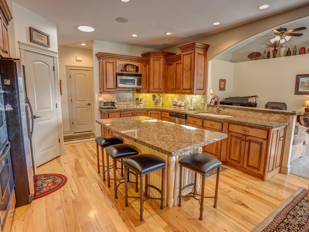 Example of a large arts and crafts u-shaped light wood floor eat-in kitchen design in Salt Lake City with raised-panel cabinets, medium tone wood cabinets, granite countertops, beige backsplash, ceramic backsplash, stainless steel appliances and an island