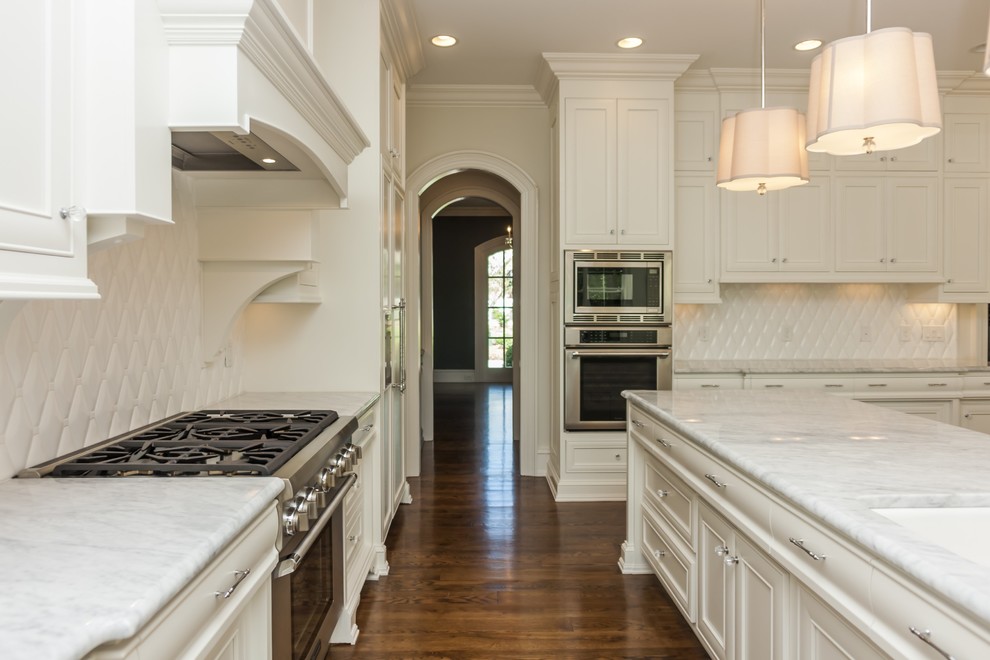 Photo of a large traditional l-shaped open plan kitchen in Raleigh with beaded cabinets, white cabinets, white splashback, stainless steel appliances and multiple islands.