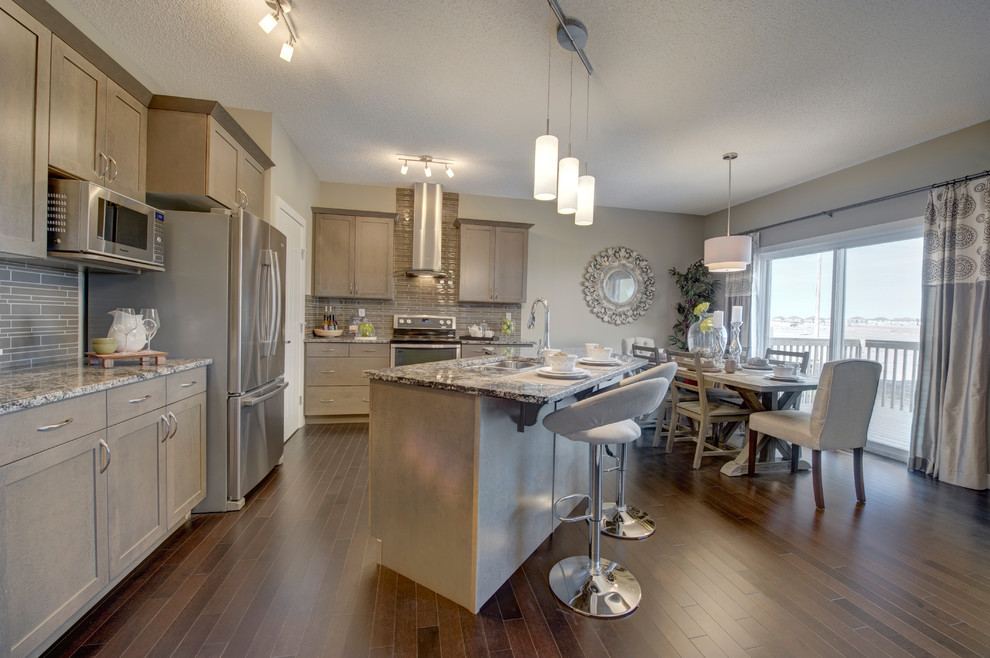 Inspiration for a mid-sized contemporary l-shaped medium tone wood floor eat-in kitchen remodel in Edmonton with an undermount sink, raised-panel cabinets, gray cabinets, granite countertops, gray backsplash, stainless steel appliances and an island