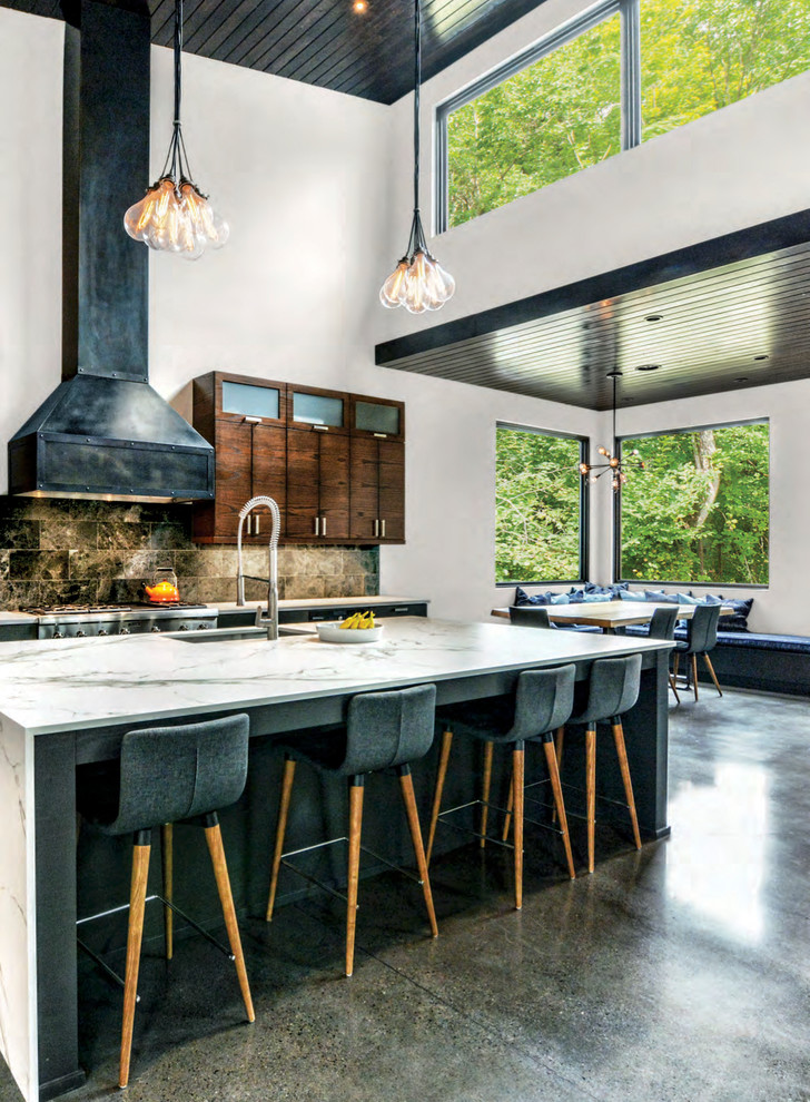Cette image montre une cuisine ouverte parallèle et bicolore urbaine en bois foncé avec un évier encastré, un placard à porte plane, une crédence noire, un électroménager en acier inoxydable, sol en béton ciré, îlot et un sol gris.