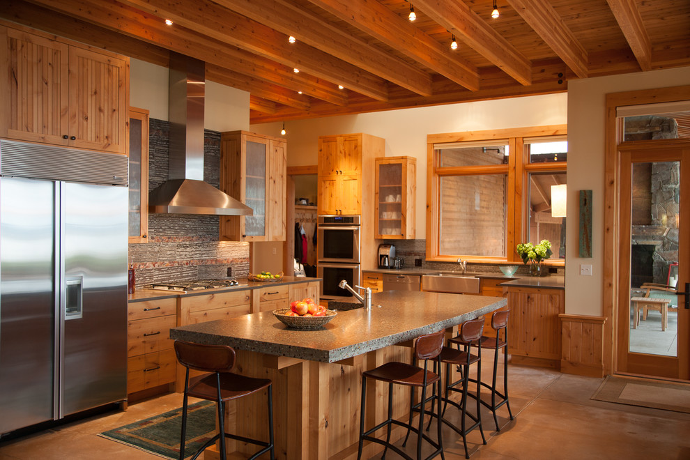 シアトルにあるラスティックスタイルのおしゃれなアイランドキッチン (エプロンフロントシンク、落し込みパネル扉のキャビネット、中間色木目調キャビネット、グレーのキッチンパネル、シルバーの調理設備、グレーの床) の写真