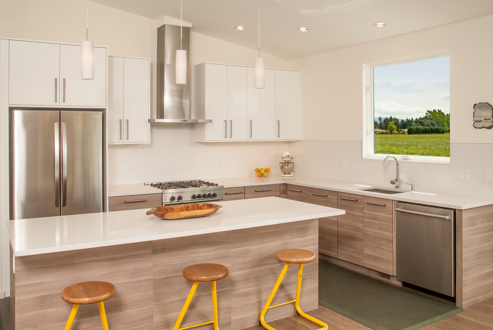 This is an example of a contemporary l-shaped kitchen in Seattle with a submerged sink, flat-panel cabinets, white cabinets, white splashback, stainless steel appliances, light hardwood flooring and an island.