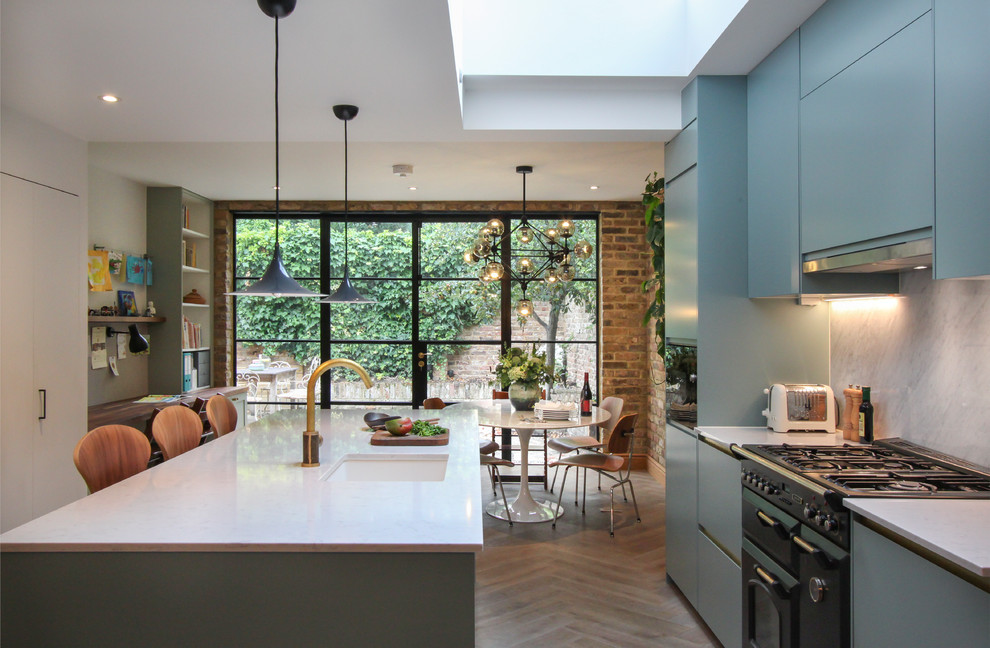 Photo of a contemporary galley kitchen/diner in London with blue cabinets, quartz worktops, white splashback, marble splashback, light hardwood flooring, a submerged sink, flat-panel cabinets, black appliances, an island and grey floors.