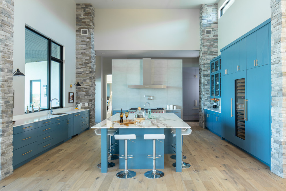 Photo of a contemporary kitchen in Austin with flat-panel cabinets, blue cabinets, grey splashback, integrated appliances, light hardwood flooring, an island, beige floors and multicoloured worktops.