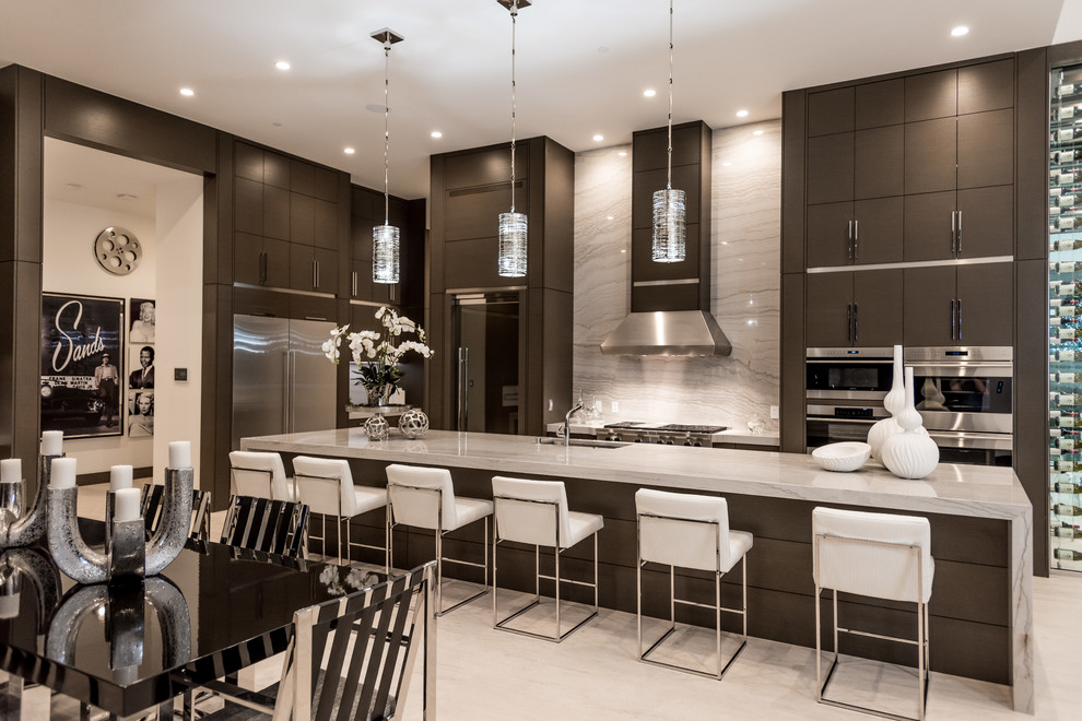 Example of a mid-sized trendy l-shaped travertine floor and gray floor open concept kitchen design in Las Vegas with an undermount sink, dark wood cabinets, granite countertops, stainless steel appliances, an island, flat-panel cabinets, white backsplash and stone slab backsplash