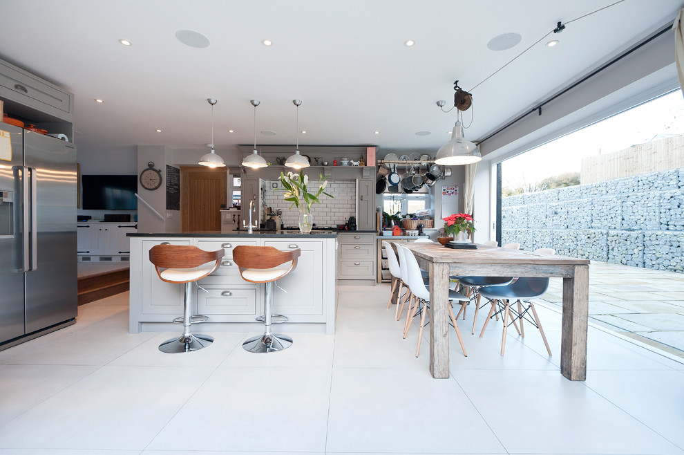 Landhaus Wohnküche in L-Form mit Schrankfronten im Shaker-Stil, grauen Schränken, Küchenrückwand in Weiß, Rückwand aus Metrofliesen, Küchengeräten aus Edelstahl und Kücheninsel in London