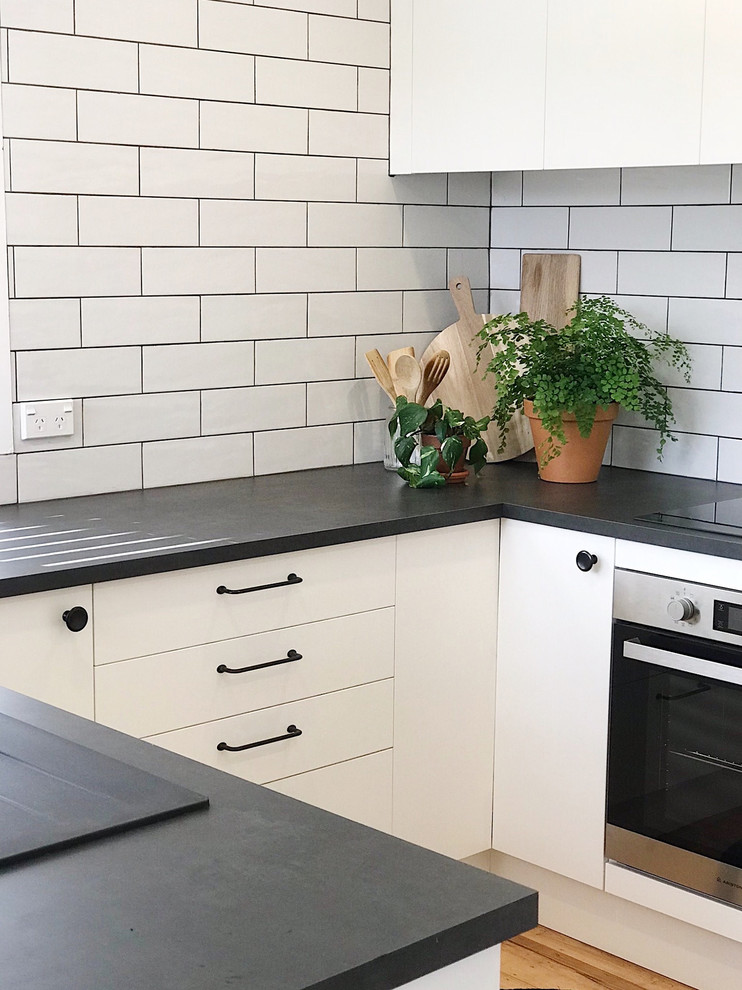 This is an example of a medium sized modern u-shaped enclosed kitchen in Auckland with a built-in sink, flat-panel cabinets, white cabinets, laminate countertops, white splashback, metro tiled splashback, medium hardwood flooring, no island and black worktops.