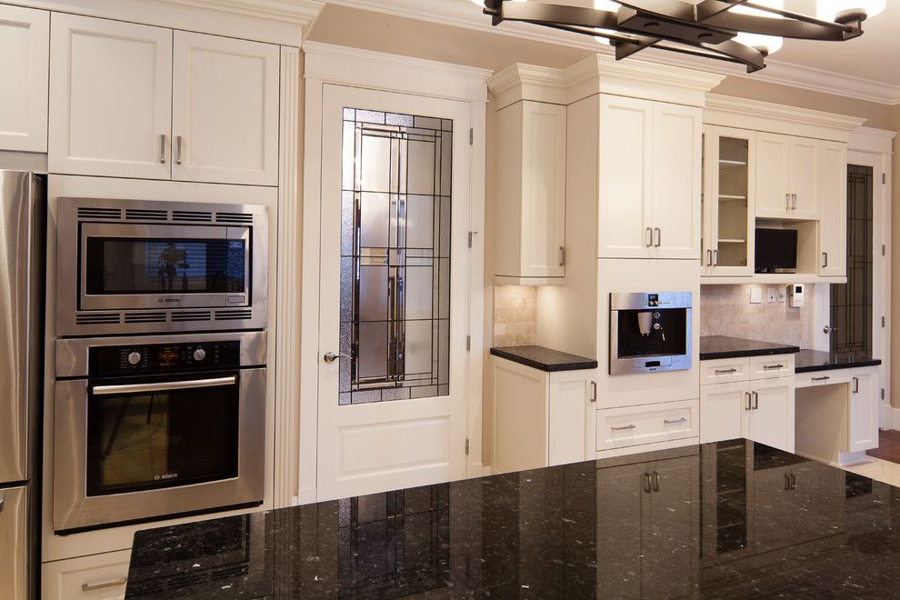 This is an example of a traditional u-shaped kitchen/diner in Vancouver with a submerged sink, white cabinets, granite worktops, beige splashback, stone tiled splashback, stainless steel appliances and recessed-panel cabinets.