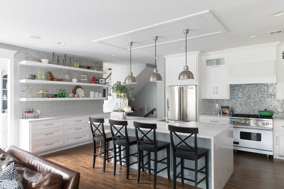 Photo of a classic l-shaped kitchen in Kansas City with a belfast sink, shaker cabinets, white cabinets, grey splashback, mosaic tiled splashback, white appliances, dark hardwood flooring, an island and brown floors.