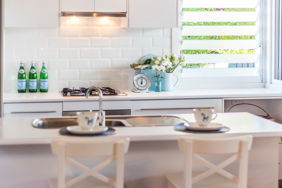 Foto di un cucina con isola centrale costiero con lavello a doppia vasca, paraspruzzi bianco, paraspruzzi in gres porcellanato, elettrodomestici in acciaio inossidabile e pavimento in legno massello medio