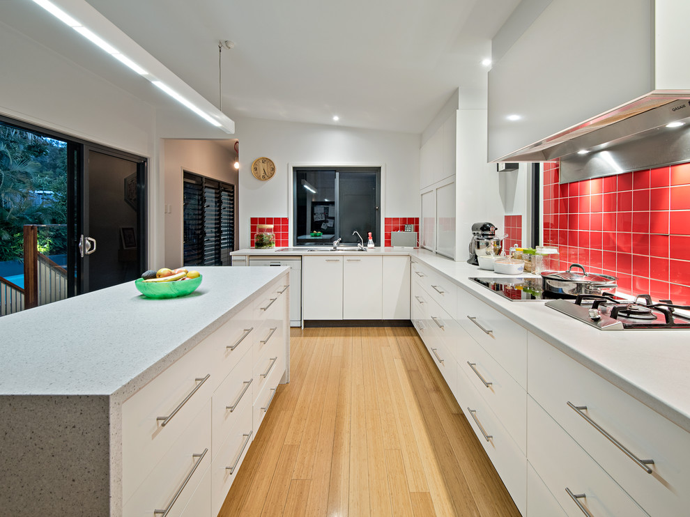 Große Moderne Wohnküche in L-Form mit Doppelwaschbecken, flächenbündigen Schrankfronten, weißen Schränken, Quarzwerkstein-Arbeitsplatte, Küchenrückwand in Rot, Rückwand aus Keramikfliesen, Küchengeräten aus Edelstahl, hellem Holzboden, Kücheninsel, beigem Boden und weißer Arbeitsplatte in Brisbane