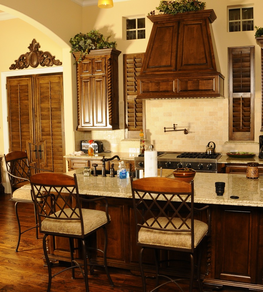 Modelo de cocina clásica con armarios con paneles empotrados, puertas de armario de madera en tonos medios, salpicadero beige, salpicadero de azulejos tipo metro y barras de cocina