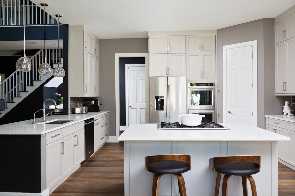 Inspiration for a medium sized traditional u-shaped kitchen/diner in Orlando with a submerged sink, shaker cabinets, grey cabinets, engineered stone countertops, grey splashback, porcelain splashback, stainless steel appliances, medium hardwood flooring, an island, brown floors and white worktops.