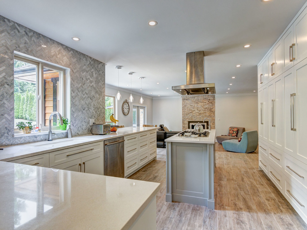 Photo of a large contemporary l-shaped kitchen/diner in Vancouver with shaker cabinets, white cabinets, granite worktops, an island, a submerged sink, grey splashback, stone tiled splashback, stainless steel appliances and porcelain flooring.