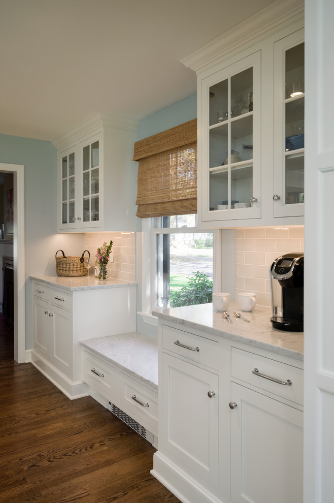 Eat-in kitchen - huge traditional l-shaped medium tone wood floor eat-in kitchen idea in Philadelphia with a farmhouse sink, recessed-panel cabinets, white cabinets, marble countertops, white backsplash, glass tile backsplash, stainless steel appliances and an island