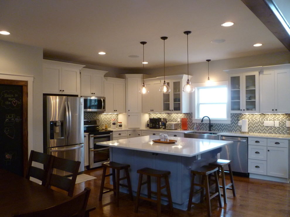 Example of a mid-sized arts and crafts l-shaped medium tone wood floor eat-in kitchen design in Nashville with a farmhouse sink, shaker cabinets, white cabinets, gray backsplash, glass tile backsplash, stainless steel appliances and an island