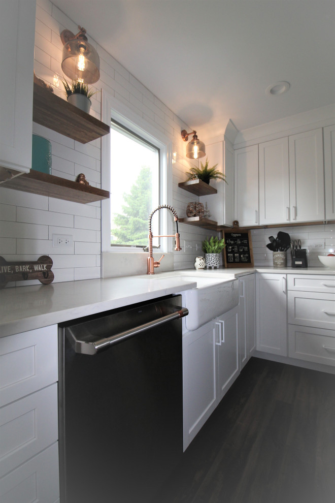 Idées déco pour une cuisine américaine romantique en L de taille moyenne avec un évier de ferme, un placard à porte shaker, des portes de placard blanches, un plan de travail en surface solide, une crédence blanche, une crédence en carreau de porcelaine, un électroménager en acier inoxydable, un sol en vinyl, îlot, un sol marron et un plan de travail blanc.