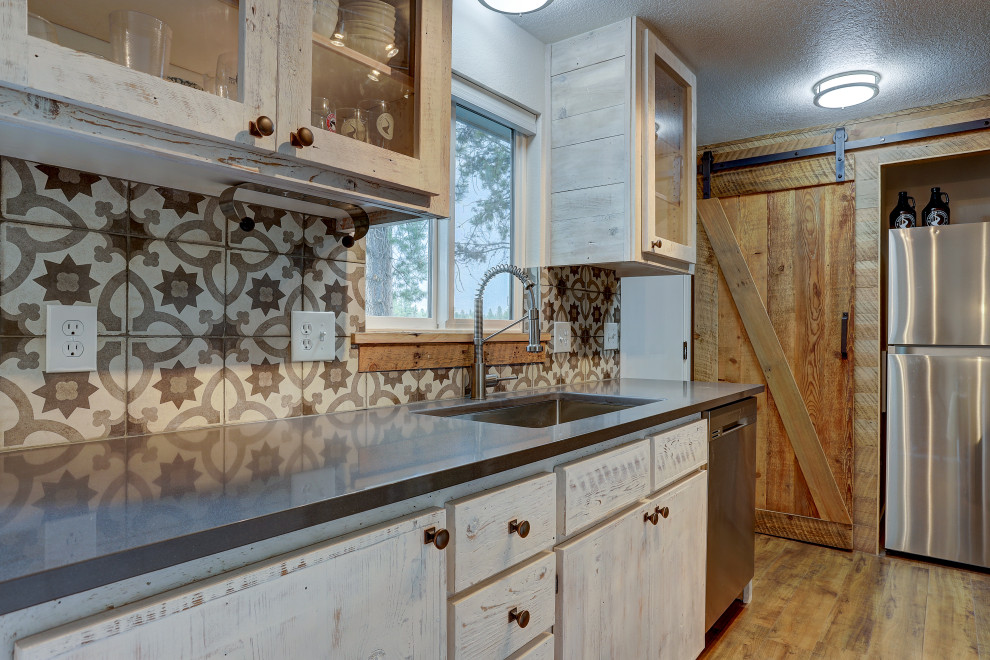Inredning av ett rustikt mellanstort svart svart kök, med en undermonterad diskho, luckor med glaspanel, flerfärgad stänkskydd, stänkskydd i keramik, rostfria vitvaror, laminatgolv, en köksö, brunt golv, skåp i slitet trä och granitbänkskiva