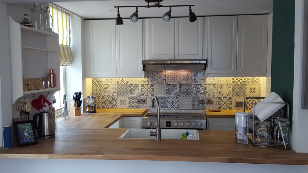 Mittelgroße Shabby-Chic Küche in U-Form mit Landhausspüle, Lamellenschränken, weißen Schränken, Arbeitsplatte aus Holz und Rückwand aus Keramikfliesen in Sonstige