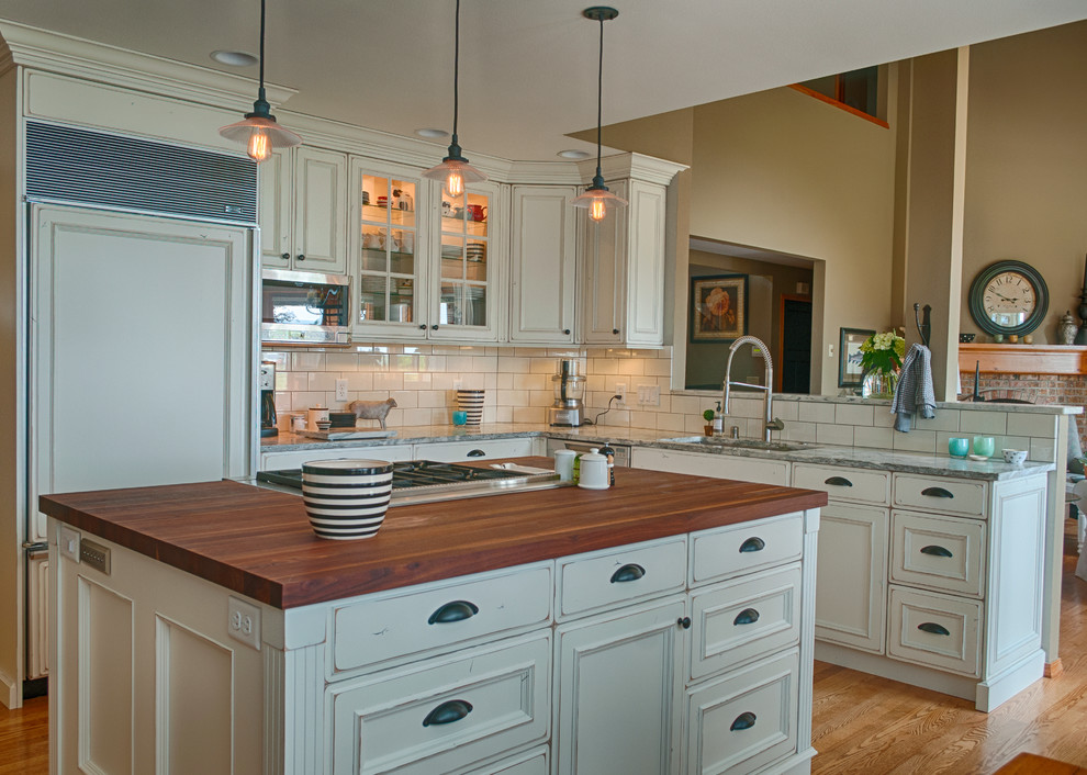 Example of a mid-sized cottage chic l-shaped light wood floor eat-in kitchen design in Seattle with recessed-panel cabinets, white cabinets, white backsplash, an island, an undermount sink, wood countertops, subway tile backsplash and paneled appliances