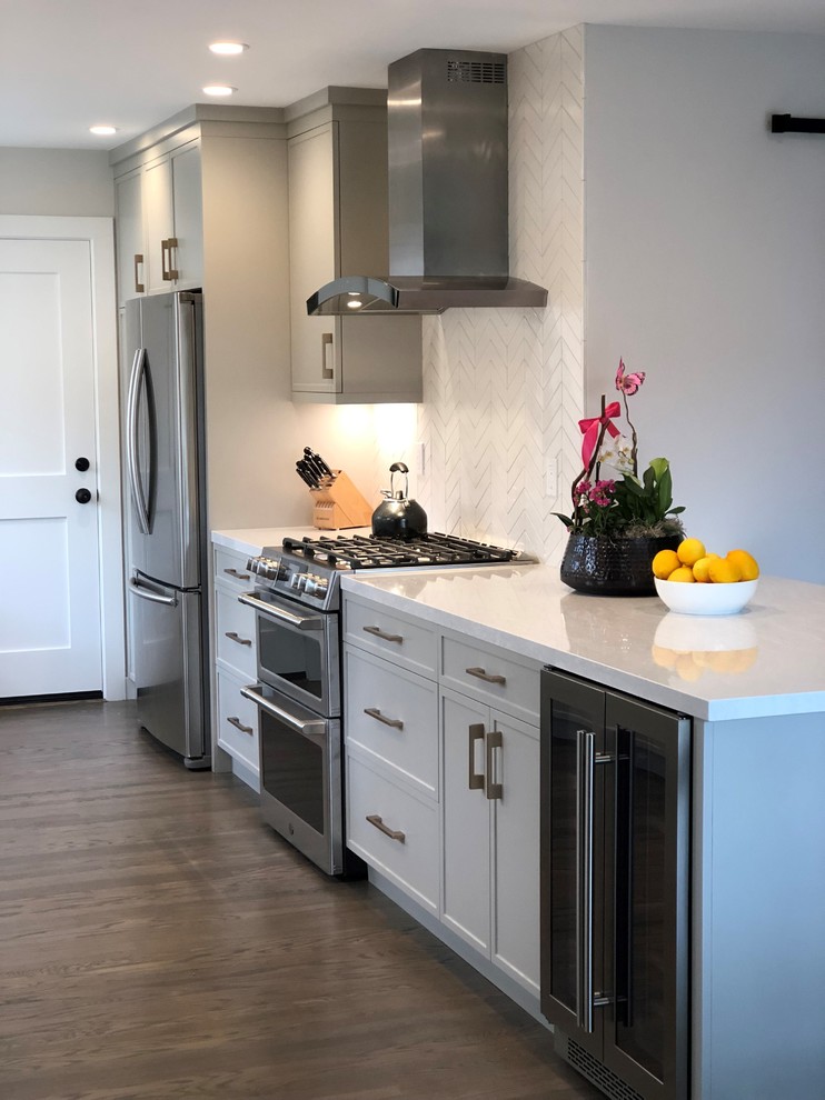 This is an example of a small traditional open plan kitchen in San Francisco with a submerged sink, shaker cabinets, engineered stone countertops, white splashback, ceramic splashback, stainless steel appliances, medium hardwood flooring, a breakfast bar, brown floors, white worktops and grey cabinets.